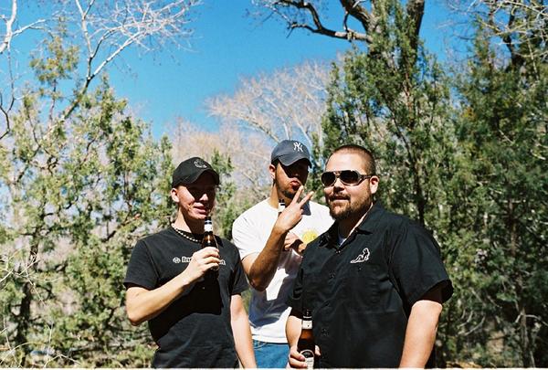 Three men with beer bottles in a wooded area