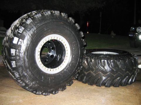 1985 Ford Bronco - Oversized off-road tires and custom wheels are displayed, with a vehicle visible in the background.