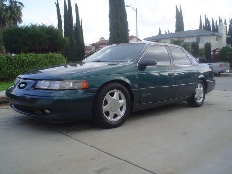 1993 Ford Taurus - A dark green 1993 Ford Taurus sedan is parked in front of a suburban house.