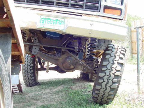 1981 Ford Bronco - The front suspension and large off-road tire of a truck are shown in detail, with a license plate mounted on the front.
