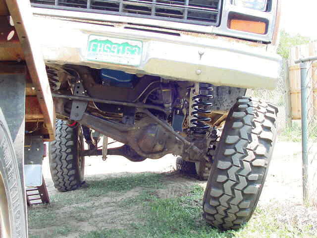 Underside front view of a lifted Ford 4x4 flexing its solid front axle and coil springs on a ramp