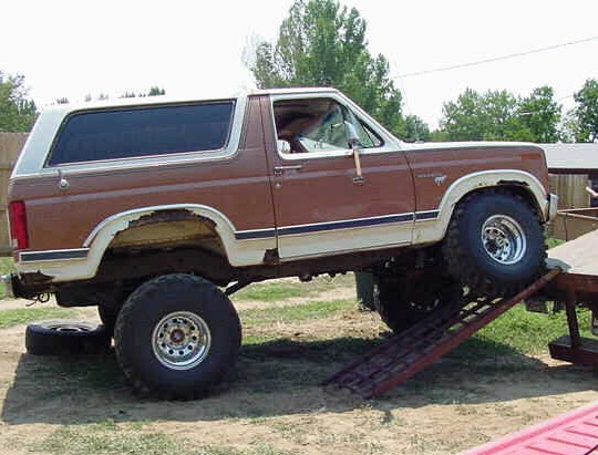 Brown and white Ford Bronco on ramps, showing rust around wheel wells