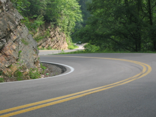 Motorcycle on a winding mountain road with trees and a rock face