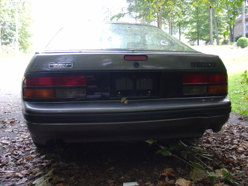 Dark gray 1986 Mazda RX-7 rear view, with a sticker on the left and "MAZDA" badging on the right