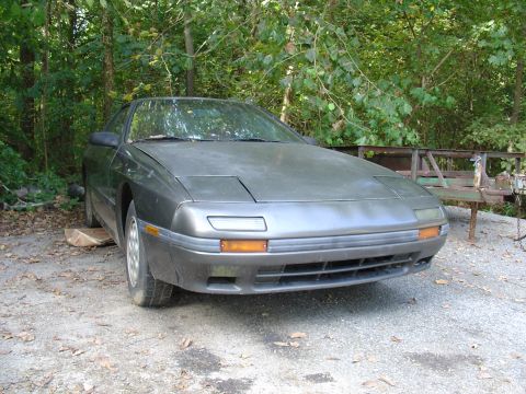 1986 Mazda RX-7 - This 1986 Mazda RX-7 is parked outdoors in a wooded area.