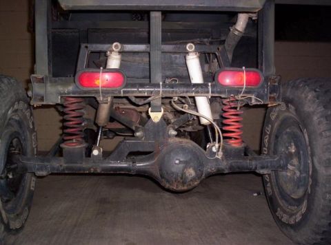 1987 Suzuki Samurai - The rear suspension and axle assembly of a vehicle are visible, red coil springs and dual shock absorbers.