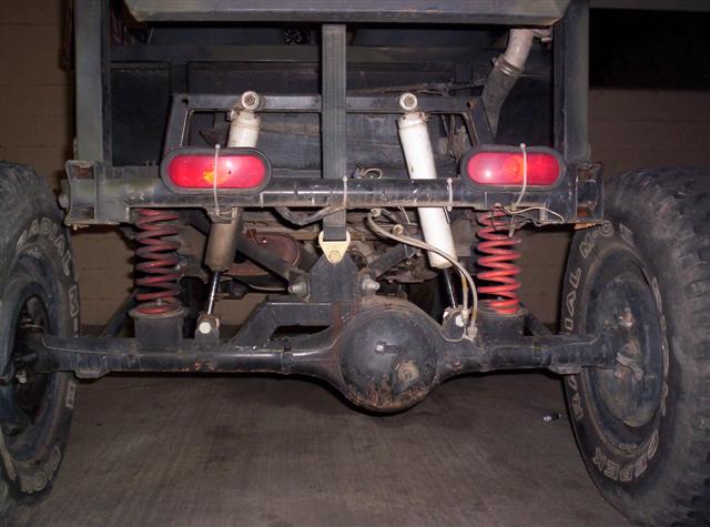 Rear axle, red coil springs, and dual shock absorbers on a vehicle with large tires