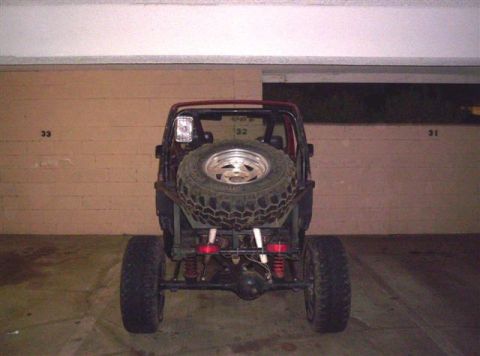 1987 Suzuki Samurai - Rear view of a modified off-road vehicle, a spare tire mounted externally. Numbers are visible on the wall behind the vehicle.