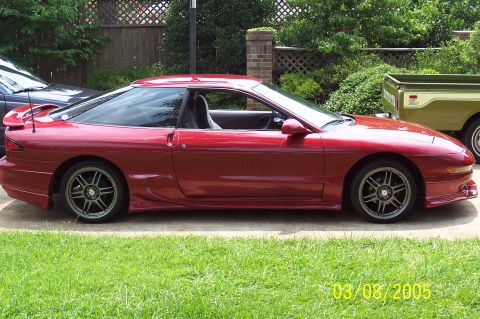1995 Ford Probe - Side profile of a red 1995 Ford Probe with aftermarket wheels, parked outdoors.