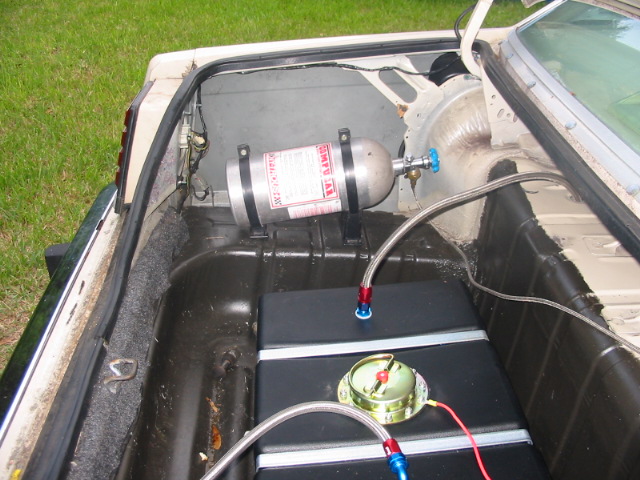 Car trunk with a nitrous oxide tank mounted above a fuel cell, connected by braided hoses