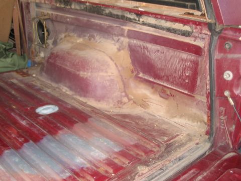 1991 Ford Bronco - The interior of a red truck bed shows a ribbed floor and a speaker cutout on the side panel.