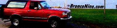 1995 Ford Bronco - Red Ford Bronco parked near water with a website address visible on a pole.