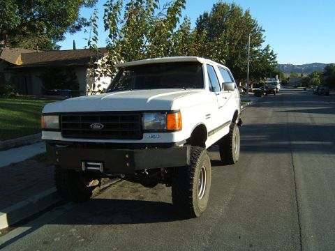 1988 Ford Bronco - A lifted white Ford Bronco sits on a residential street under a clear blue sky.