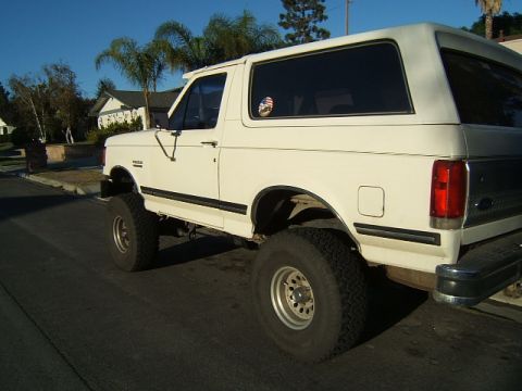 1988 Ford Bronco - A white 1988 Ford Bronco is shown from the rear 3/4 angle, a lifted suspension and large off-road tires.