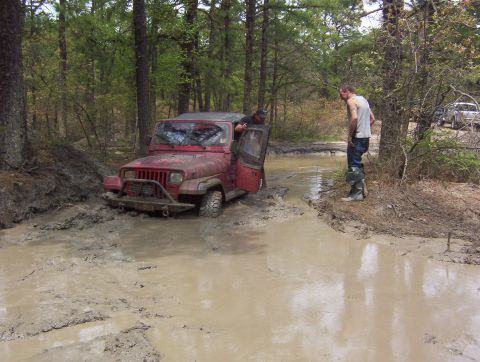2005 Dodge 1500 - A red Jeep is stuck in the mud while two men stand nearby, with another vehicle in the background.