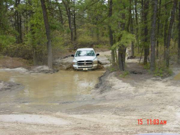 White 2005 Dodge 1500 driving through mud puddle. Front view