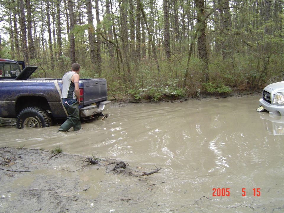 Blue pickup truck stuck in mud, with a silver truck visible in the background