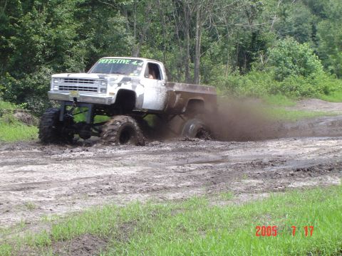 2005 Dodge 1500 - A heavily modified pickup truck is shown navigating a muddy off-road course, with its tires deep in the muck.