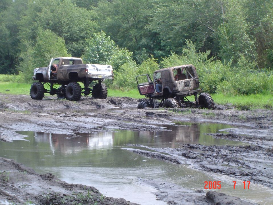 Lifted 1980s pickup truck and a lifted Jeep Wrangler stuck in mud, side view