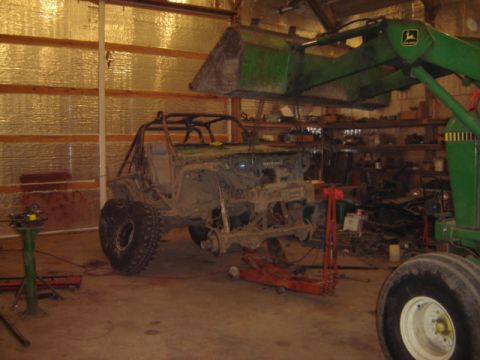 1992 Ford Bronco - Off-road vehicle undergoing modification in a workshop with a tractor loader above.
