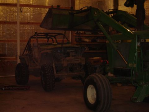 1992 Ford Bronco - An off-road vehicle sits in a garage next to a large green tractor.