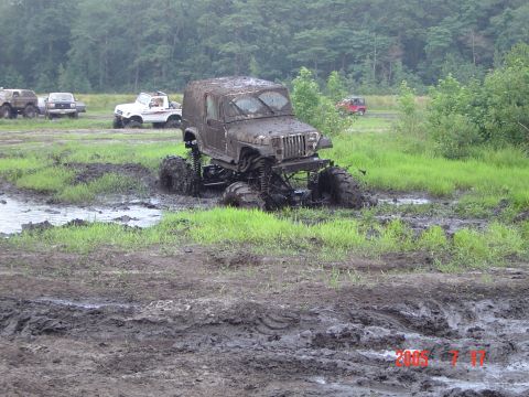 2005 Dodge 1500 - Multiple off-road vehicles navigate a muddy terrain with dense trees in the background.