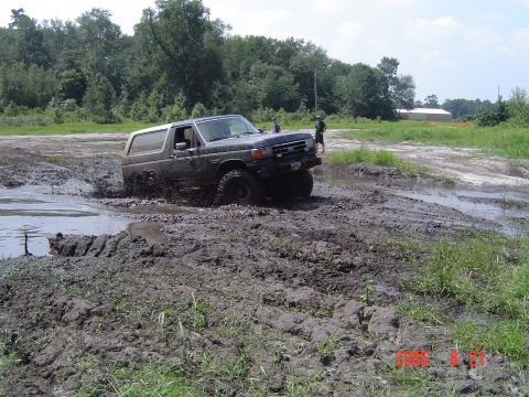 2005 Dodge 1500 - A dark SUV navigates a muddy off-road course, kicking up water and mud.
