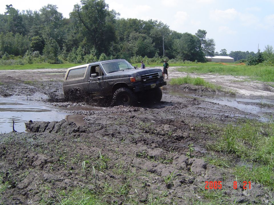 Dark SUV with off-road tires splashing mud, front-right wheel deep in water