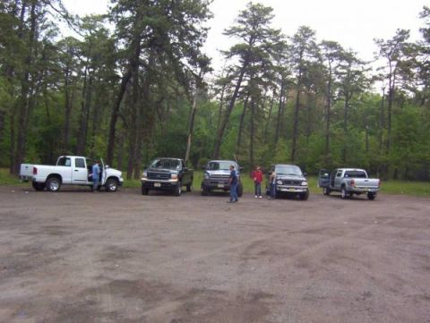 2005 Dodge 1500 - A group of pickup trucks are parked in a dirt lot surrounded by trees.