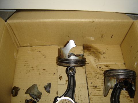 1988 Ford Bronco - Destroyed engine internals laid out in an oil-stained cardboard box: a piston with most of its crown blown away still attached to its conne…
