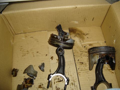 1988 Ford Bronco - Two failed pistons still bolted to their connecting rods sitting in a greasy cardboard box, one with the crown and ring lands blown apart a…