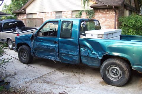 1987 Ford Bronco - Two pickup trucks are parked in a driveway, one with significant damage to its side.