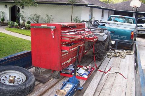 1987 Ford Bronco - A red toolbox and an ATV are loaded onto a trailer, with a teal Chevrolet pickup truck visible in the background.