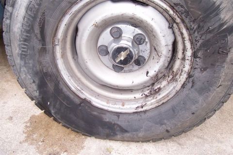 1987 Ford Bronco - A close-up view of a flat tire and a damaged wheel with a Chevrolet emblem.