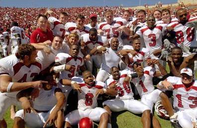 1996 Ford Mustang - A football team celebrates on the field in front of a large crowd in the stands.