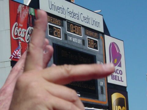 1996 Ford Mustang - A scoreboard displays game information and advertisements, with a hand obscuring part of the view.