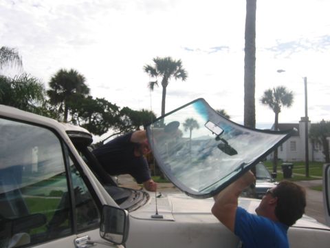1989 Ford Bronco - A new windshield is being fitted into a vehicle's frame by two individuals.