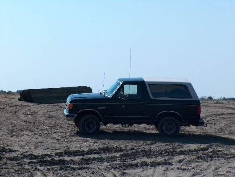1991 Ford Bronco - A black and white 1991 Ford Bronco is parked on a dirt lot under a clear blue sky.