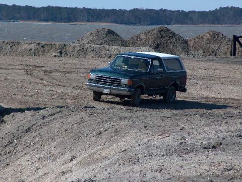 1991 Ford Bronco - Dark green 1991 Ford Bronco with a white top sits on a dusty, uneven terrain.