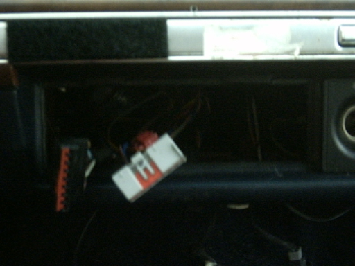 Empty car radio dash opening with factory wiring harness and adapter plugs hanging out