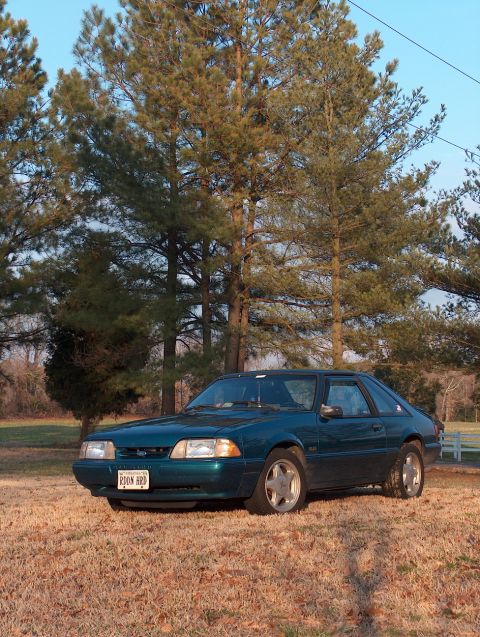 1993 Ford Mustang - A teal 1993 Ford Mustang coupe is shown from a 3/4 front angle, parked outdoors on a dry, grassy field.