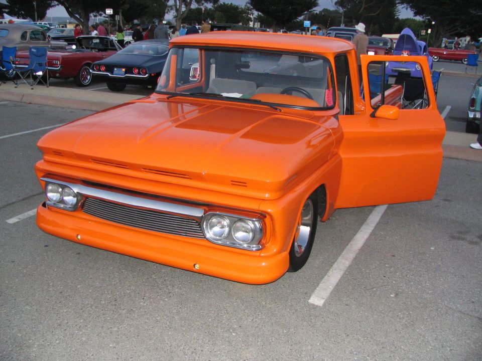 Orange pickup truck with driver's door open, chrome grille, and dual headlights