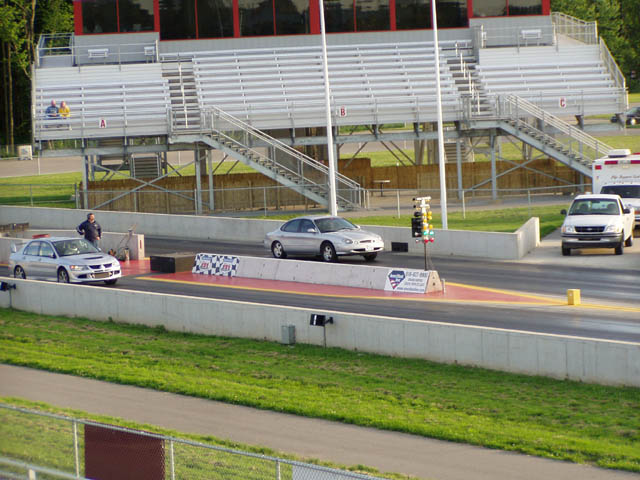 Silver sedan on drag strip with a white pickup truck in background