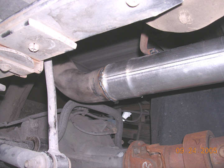 Freshly welded large-diameter exhaust pipe under a truck, driveshaft u-joint in foreground