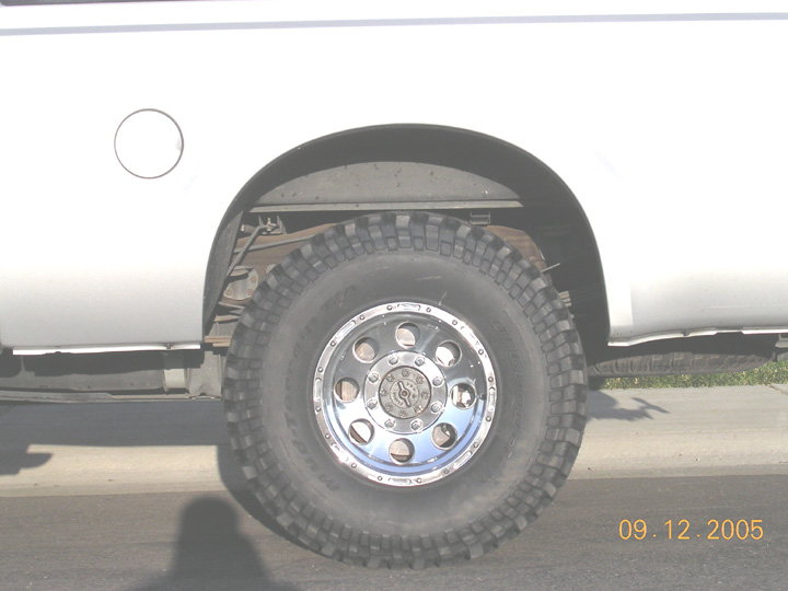 Mud-terrain tire on polished eight-lug wheel under the rear fender of a white pickup