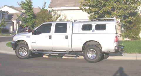 2004 Ford F-250 - This silver pickup truck appears to be a 2004 Ford F-250, equipped with a camper shell and roof rack.