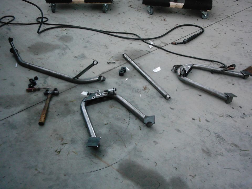 Several metal motorcycle kickstands and parts laid out on a concrete floor with tools