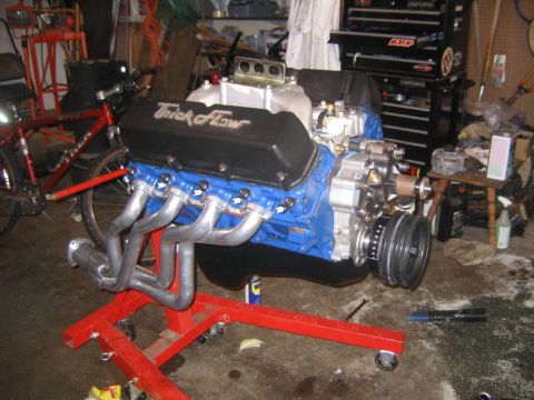 1978 Ford Bronco - A Ford V8 painted Ford blue on a red engine stand in a garage, fitted with black Trick Flow valve covers, long-tube stainless headers, a po…