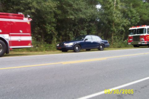 1998 Ford Crown Victoria - A dark blue 1998 Ford Crown Victoria is parked on the side of the road next to a fire truck.