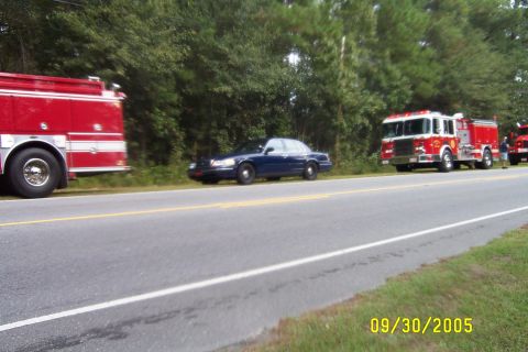 1998 Ford Crown Victoria - A blue 1998 Ford Crown Victoria is parked on the side of a road with two fire trucks nearby.